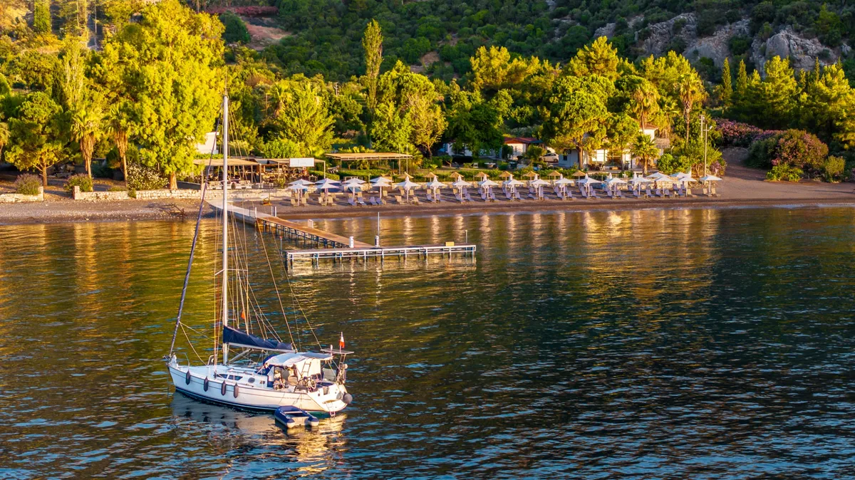 Altın saatte koy: demirlemiş yelkenli, iskele ve hasır şemsiyeler