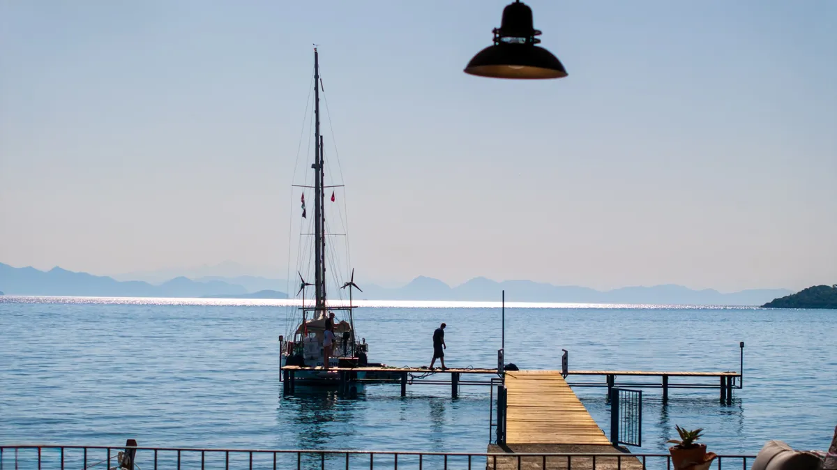Teras korkuluğunun ardından iskele, bağlı tekne ve karşı kıyının silueti