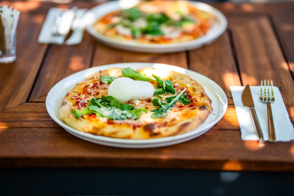 Ahşap masada roka ve taze peynirli iki pizza